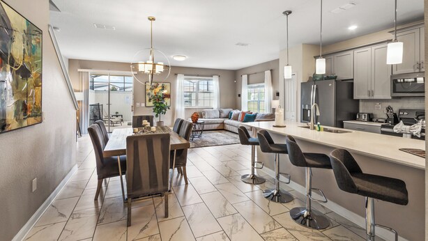 A modern kitchen with a dining area, featuring a large island with bar stools, a built-in oven, and a refrigerator.