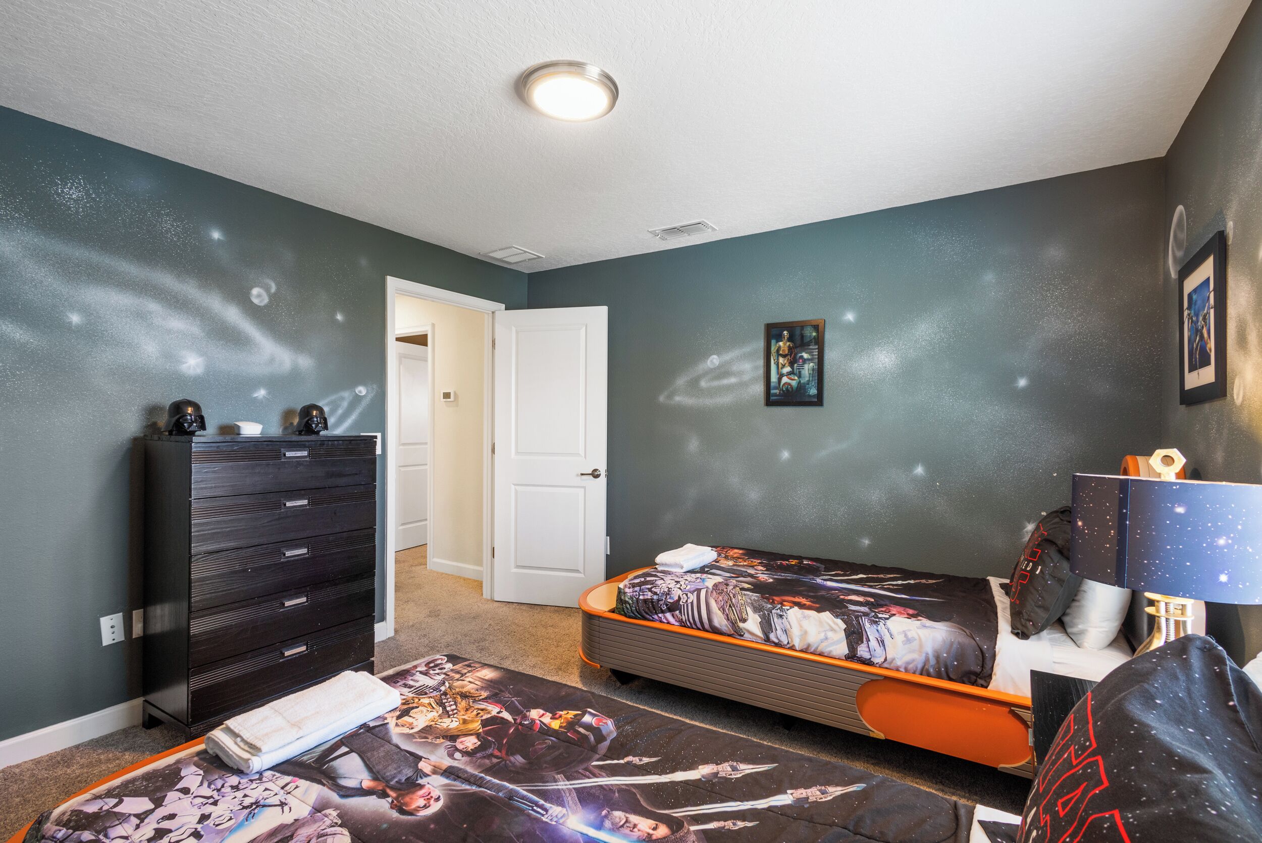 A bedroom with a bed, dresser, and a door leading to another room.