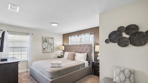 A bedroom with a large bed, a dresser, a nightstand, and a wall-mounted lamp.