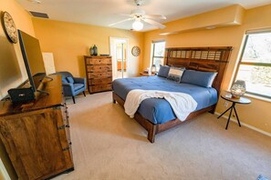 A bedroom with a large bed, a wooden dresser, a desk with a computer, a chair, and a window with a view. - Indian Cliffs Getaway ~ 3 bedroom with pool (Sedona)