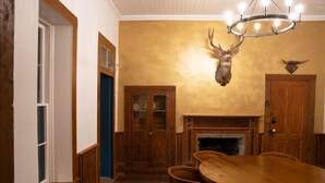 Ein Esszimmer mit Holztisch und -stühlen, einem Kamin und einem aufgehängten Hirschkopf an der Wand.