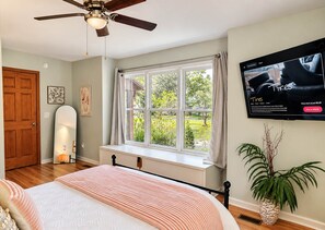 A bedroom with a bed, a ceiling fan, a window with curtains, a wall-mounted TV, and a potted plant. - Big Red Columbia Living near DT, USC, Ft. J! Pets! (West Columbia)