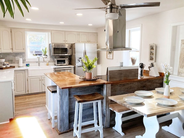 A modern kitchen with white cabinets, stainless steel appliances, a wooden island, and a dining area with white chairs.