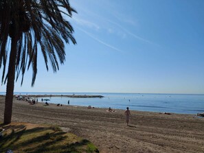 Ein Strand mit Palmen, badenden Personen und blauem Himmel.