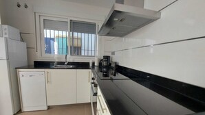 Cozinha moderna com armários brancos, bancada preta, lava-louças embutida e janela com grades.