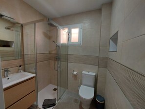 Ein modernes Badezimmer mit Duschkabine aus Glas, Toilette und Waschbecken mit Spiegel.