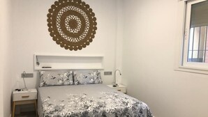 Quarto com uma cama, duas mesas de cabeceira, um objeto decorativo na parede e uma janela.