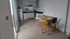 Uma cozinha compacta com armários brancos, micro-ondas, cafeteira e mesa de jantar com cadeiras.