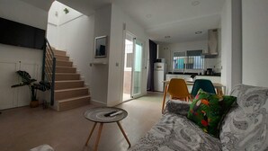 Um apartamento moderno com escada, sala de estar com sofá estampado, uma mesa redonda pequena e uma área de cozinha.