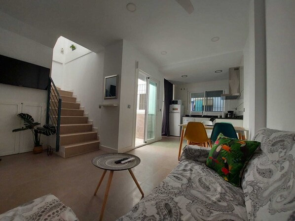 Eine moderne Wohnung mit Treppe, einem Wohnzimmer mit gemustertem Sofa, einem kleinen runden Tisch und einer Küchenzeile.