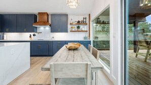 A modern kitchen with dark blue cabinets, a wooden island, and a large window overlooking a deck.