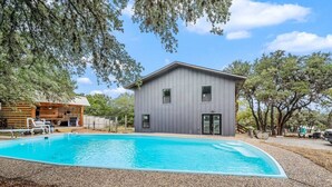 A modern house with a swimming pool, surrounded by trees and a wooden deck.