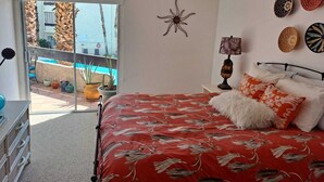 Une chambre avec un lit, un ventilateur de plafond, une table de chevet et une vue sur une piscine et un espace extérieur.