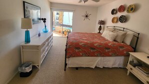 Une chambre à coucher comprenant un lit, une commode, une table de chevet, un ventilateur de plafond et une vue sur l’extérieur.