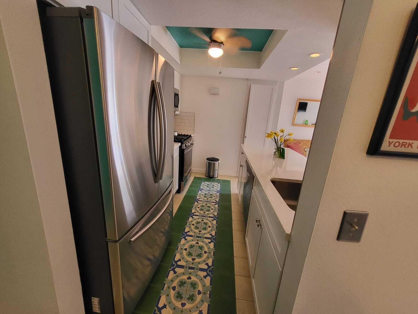 A narrow kitchen with a stainless steel refrigerator, a stove, and a ceiling fan.