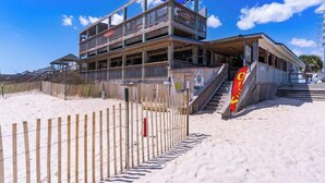 A multi-story building with balconies, a sandy beach in the foreground, and a clear blue sky. - Townhome w/ Pool & Water Views/ Sleeps 12 (Surf City)