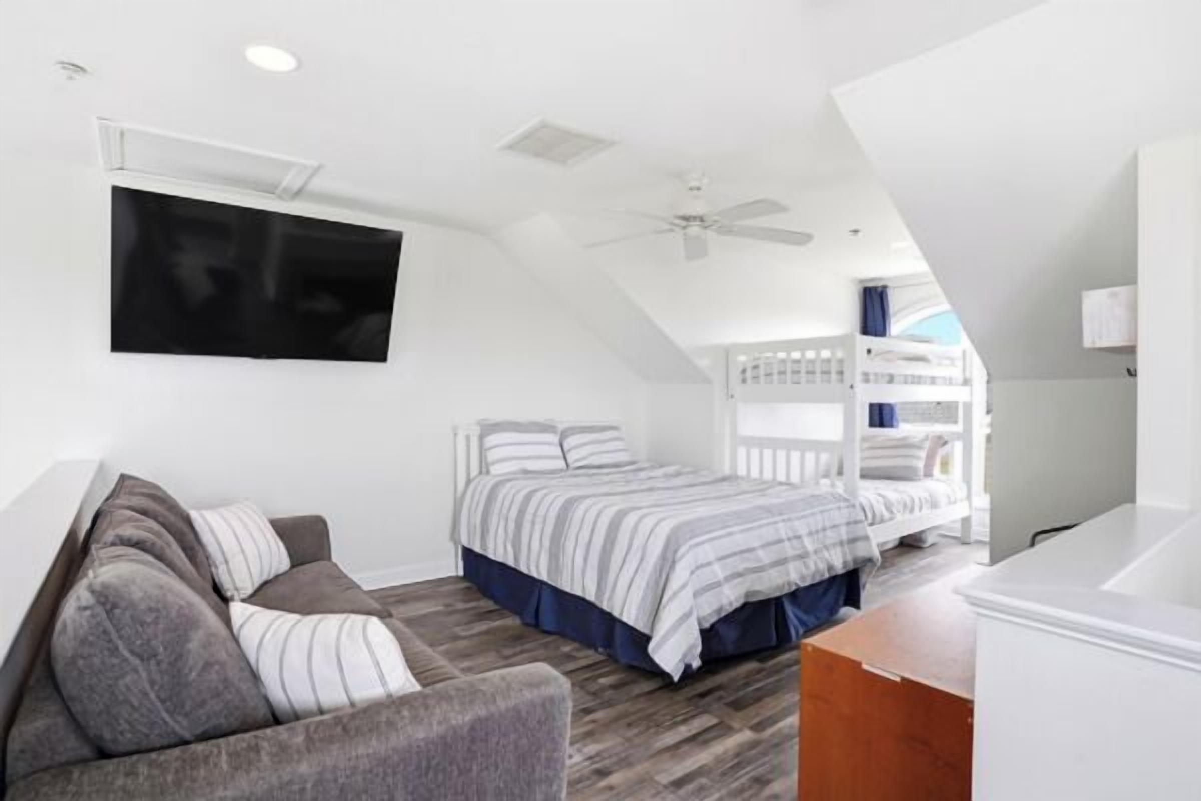 A bedroom with a bunk bed, a sofa, a flat-screen TV, and a ceiling fan.