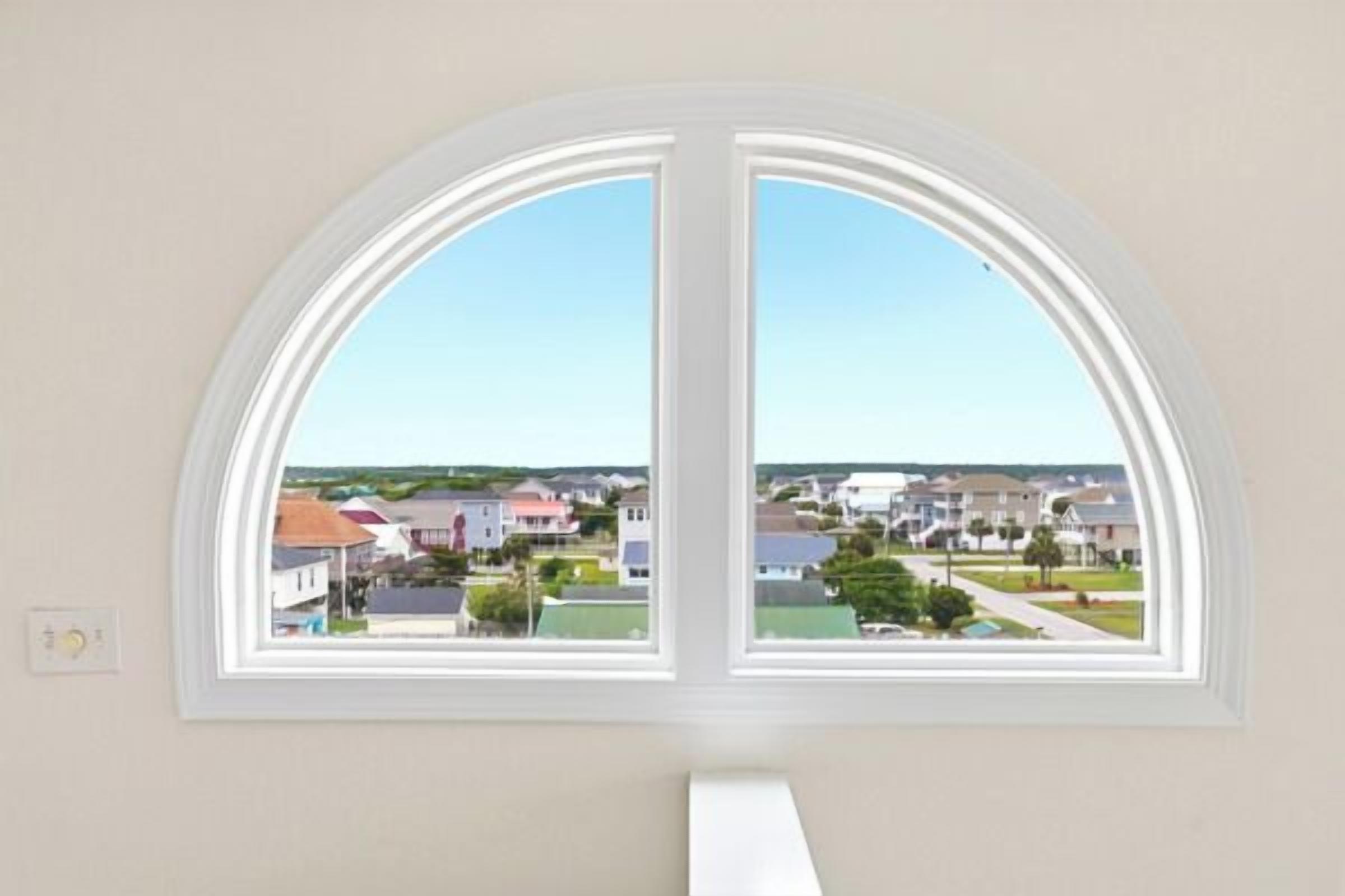 A room with a large arched window overlooking a residential area.