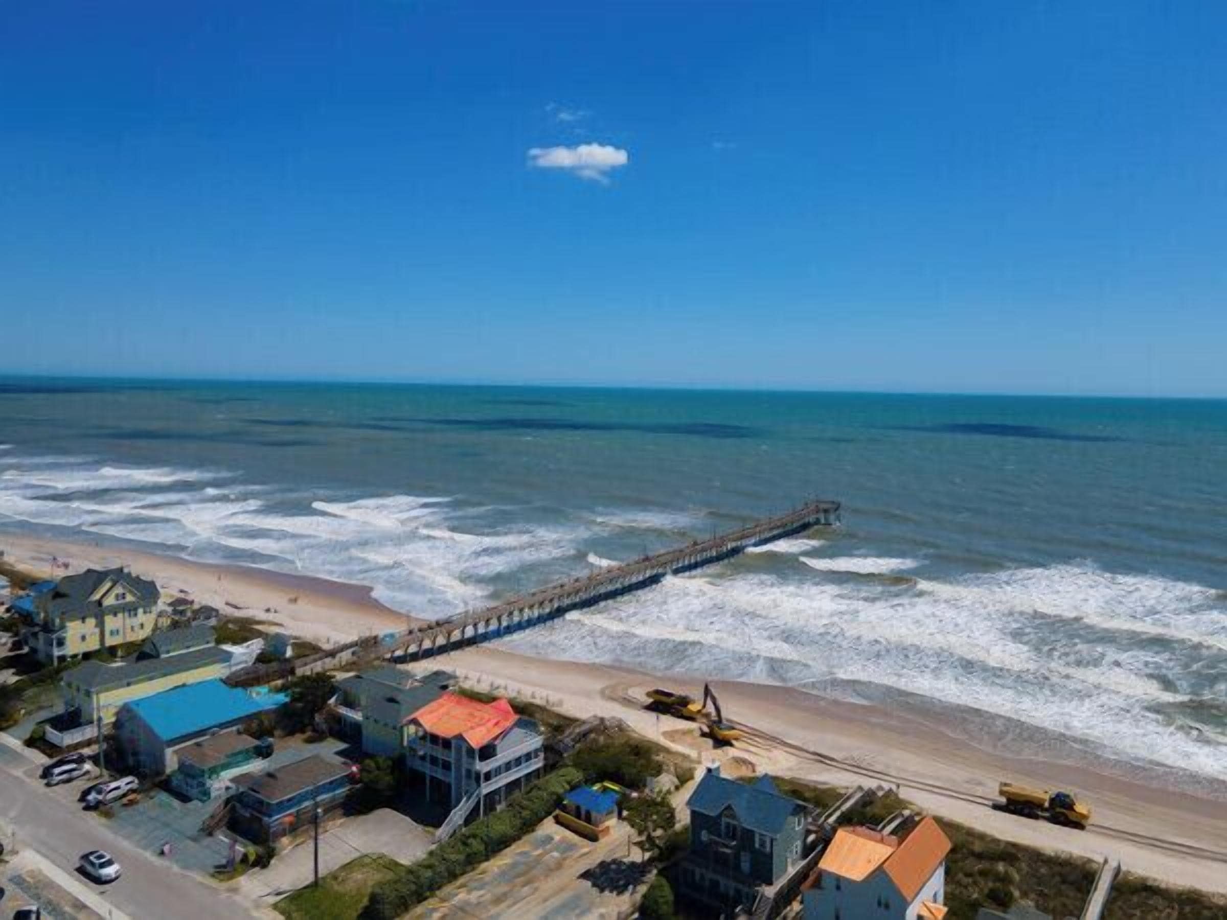 Une ville côtière avec une jetée qui s’avance dans la mer, des maisons le long de la plage et un ciel dégagé.