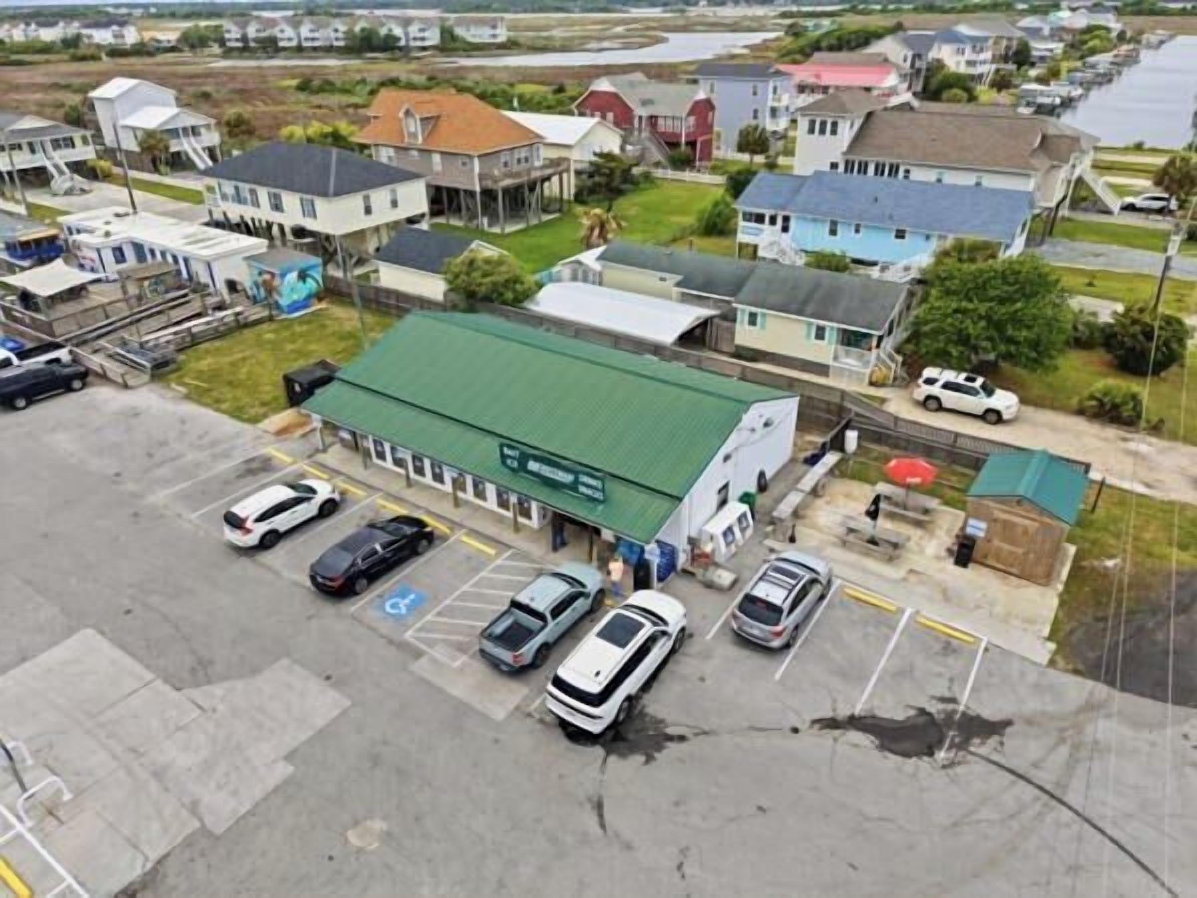 A building with a green roof, a parking lot with several cars, and a small adjacent structure.