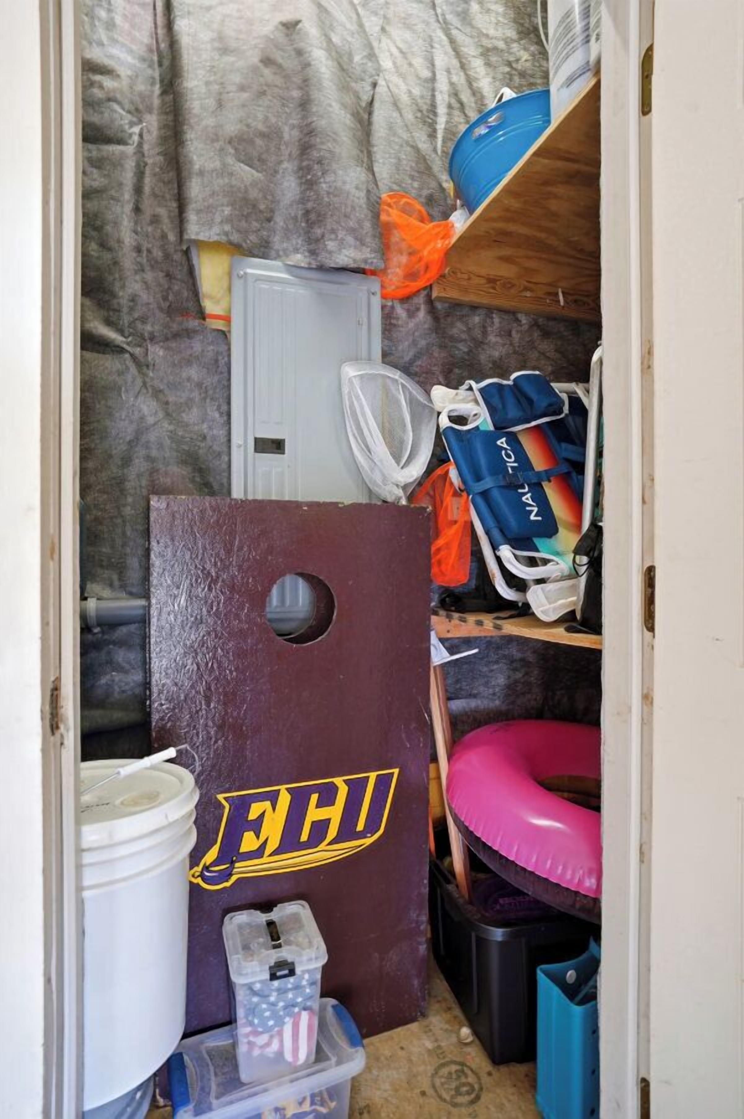 A small, cluttered room with a wooden door, a white bucket, a plastic container with an American flag, and a pink inflatable ring.