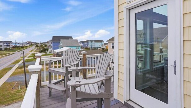 A deck with chairs, a glass door, and a view of houses. - Townhome w/ Pool & Water Views/ Sleeps 12 (Surf City)