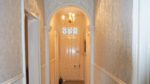 Stunning hallway with patterned wallpaper and a decorative archway above the door, featuring a chandelier and a wooden door with a glass panel.