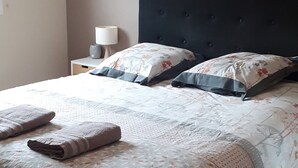 A neatly made bed with floral bedding, a dark headboard, and a wall-mounted painting of a rose.