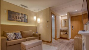 Una habitación de hotel moderna con sofá, reposapiés y un cuadro en la pared.