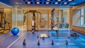 Un gimnasio con equipo de ejercicio, piso azul y un ventanal grande.