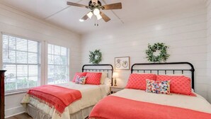 A bedroom with two beds, white walls, a ceiling fan, and a window with blinds.