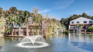 A serene water body with a fountain, surrounded by palm trees and residential buildings. - 2BR Forest Ridge condo with pool, balcony, WiFi, and beach access (Fernandina Beach)