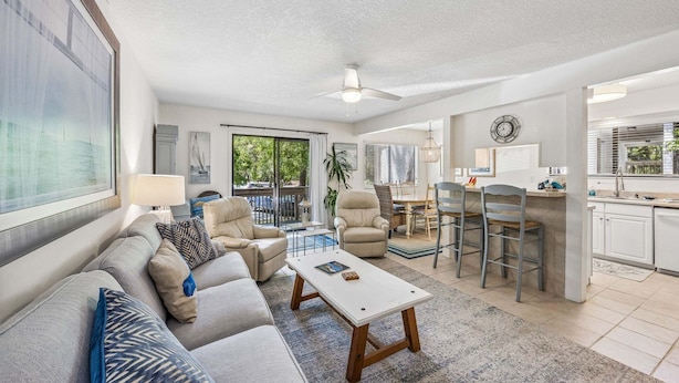 A modern living room with a sofa, coffee table, and chairs, a dining area with a table and chairs, and a kitchen with cabinets and a window. - 2BR Forest Ridge condo with pool, balcony, WiFi, and beach access (Fernandina Beach)