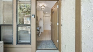 A hallway with a door, a light fixture, and a small table with chairs. - 2BR Forest Ridge condo with pool, balcony, WiFi, and beach access (Fernandina Beach)