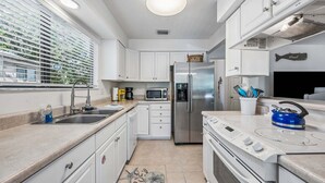 A modern kitchen with white cabinets, stainless steel appliances, a microwave, a refrigerator, and a blue kettle on the stove. - 2BR Forest Ridge condo with pool, balcony, WiFi, and beach access (Fernandina Beach)
