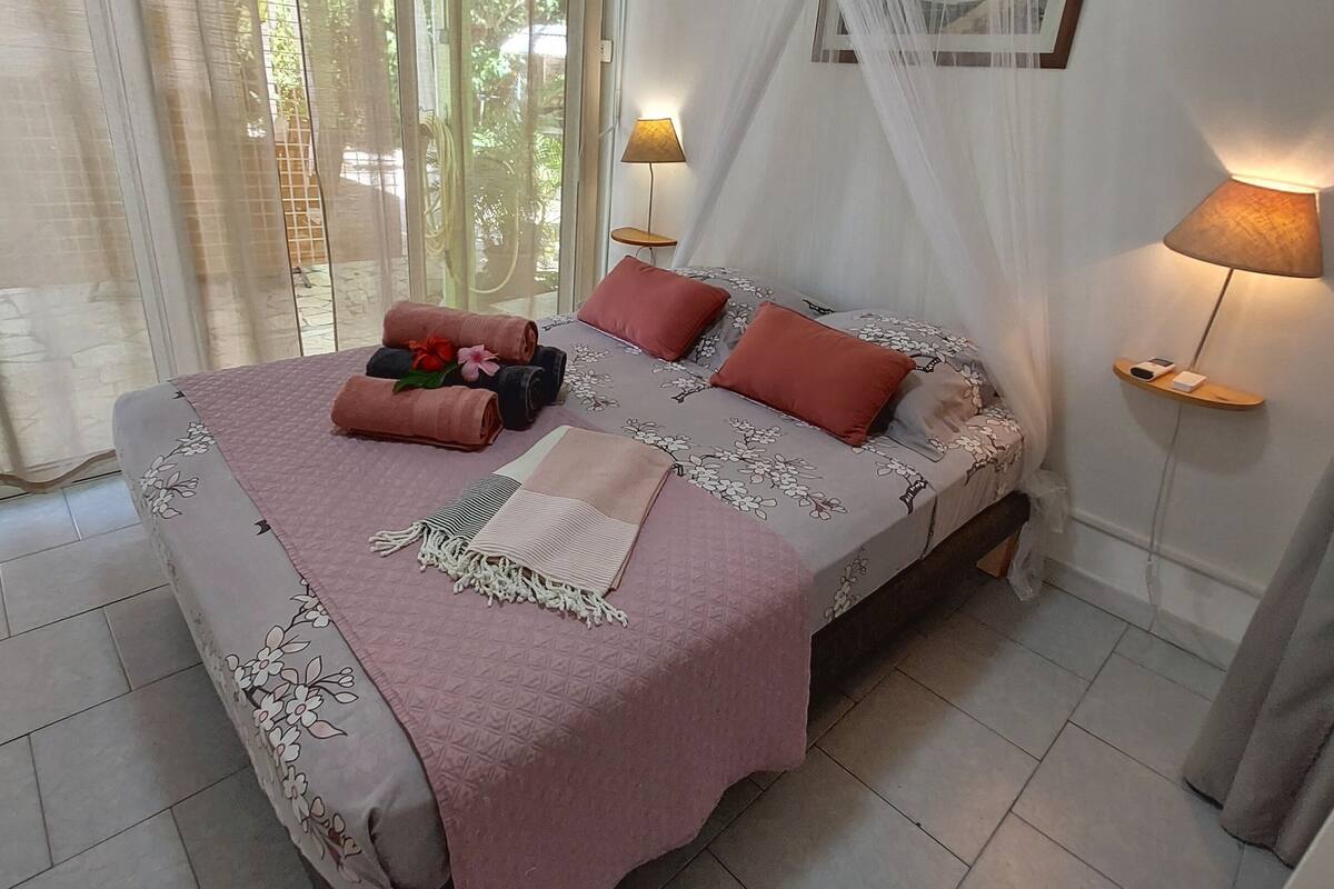 A neatly made bed with a floral bedspread, two pillows, and a rolled towel. There are two bedside lamps and a framed picture on the wall.