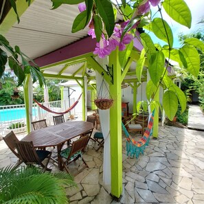 Une terrasse couverte avec une table et des chaises en bois, un hamac et une plante suspendue.