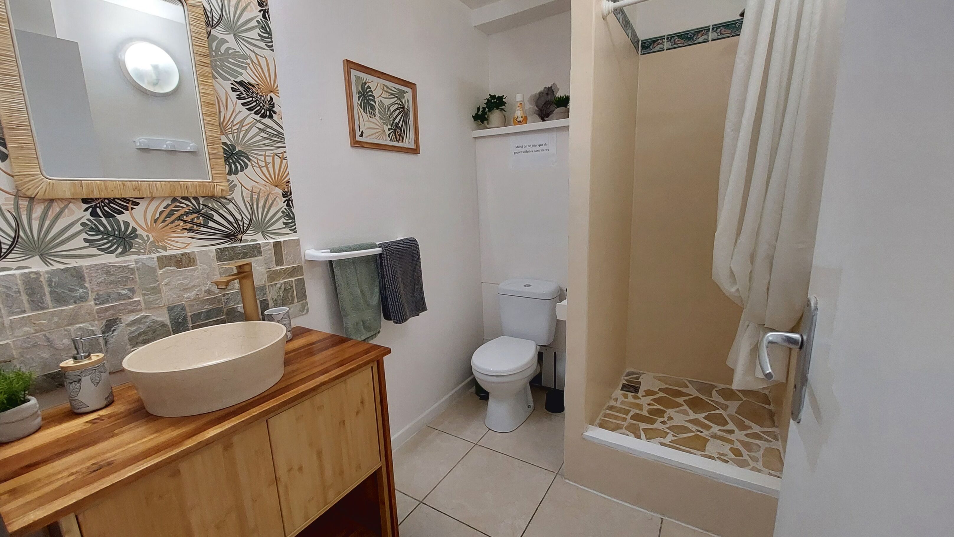 A bathroom with a wooden vanity, a large mirror, a toilet, and a shower with a tiled floor.