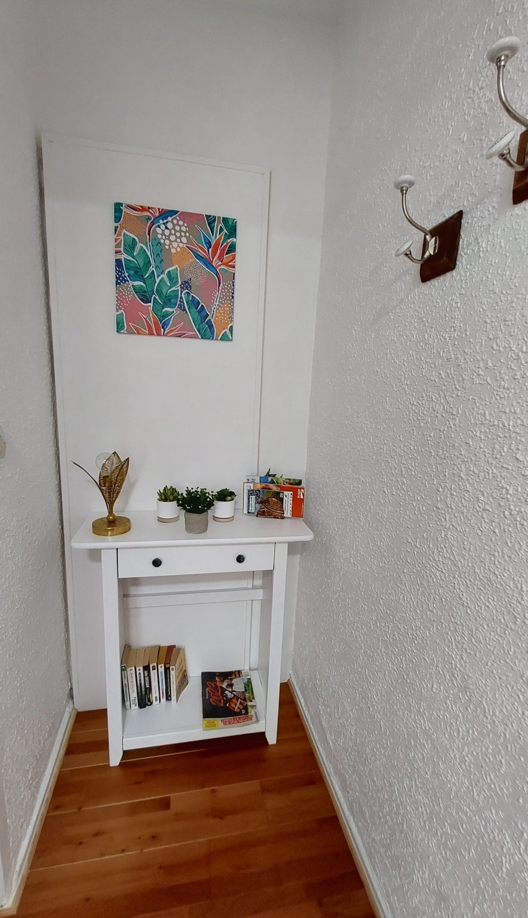 Ein weißer Konsolentisch mit einer dekorativen Blattform-Skulptur, zwei Topfpflanzen und einer kleinen Schachtel.