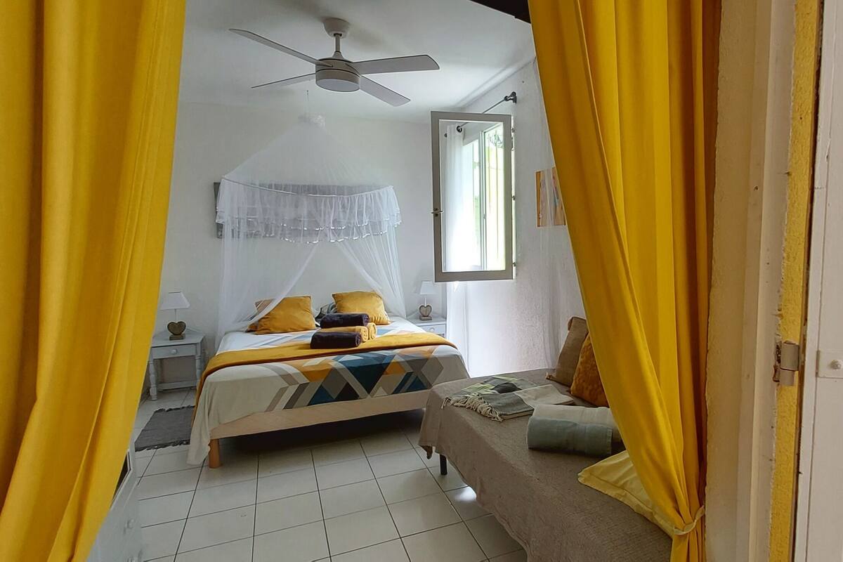 A bedroom with a bed, a nightstand, a bedside table, a window, and a ceiling fan.