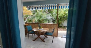 A patio area with a round wooden table and four chairs, a small fruit bowl on the table, and a bamboo fence in the background.