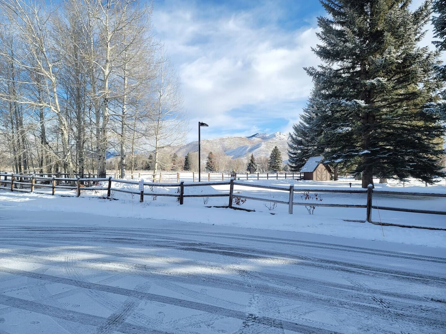 A snow-covered landscape with a wooden fence, a mountain in the background, and a clear sky.