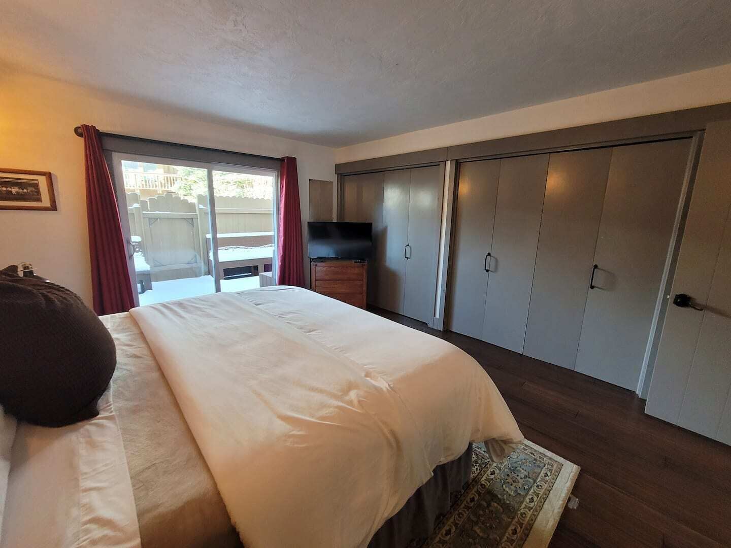Un dormitorio con una cama grande, televisión, armario y puerta corredera a un balcón.