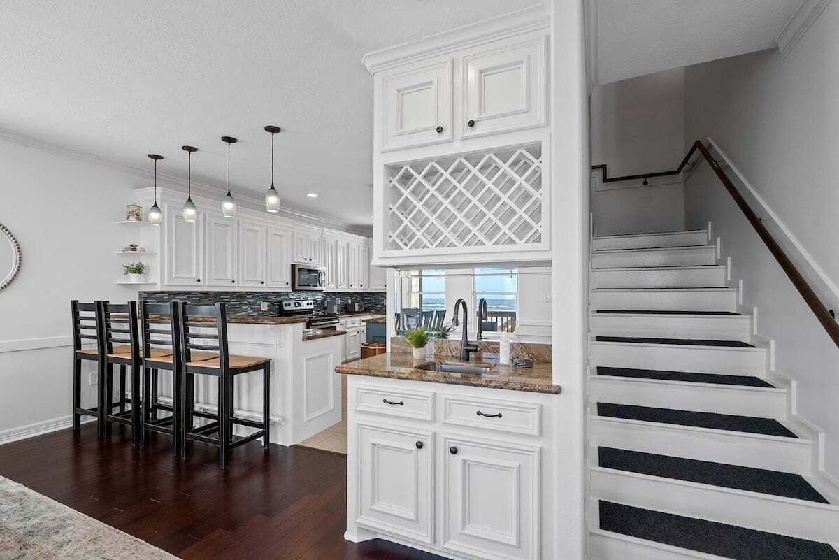 A modern kitchen with white cabinetry, a central island, and a staircase leading to a balcony.