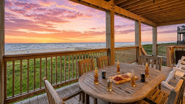 Een houten terras met een gedekte tafel, met uitzicht op de zee tijdens de zonsondergang.