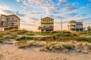 Una propiedad frente a la playa con varias construcciones, incluyendo una casa amarilla con balcón y un edificio más grande también con balcón.