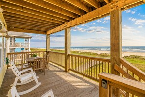 Terraza de madera con mesa y sillas, con vista a la playa.