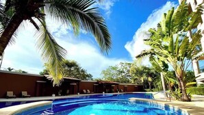 A circular pool with clear blue water, surrounded by palm trees and lounge chairs. - Peninsula 12, 𖠁 3Bdr Lux Beach condo 𖠁Pools 𖠁Rooftop 𖠁Gym 𖠁 (Playa Langosta)