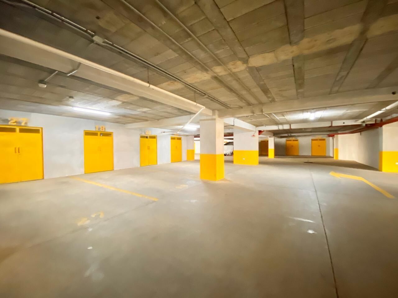 A parking garage with yellow pillars and doors, concrete floors, and overhead lighting.