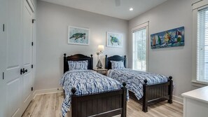 A bedroom with two beds, a window with blinds, and artwork on the walls.